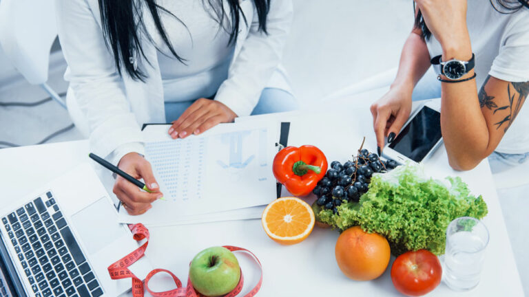Nutritionist working with patient in front of healthy foods and a computer