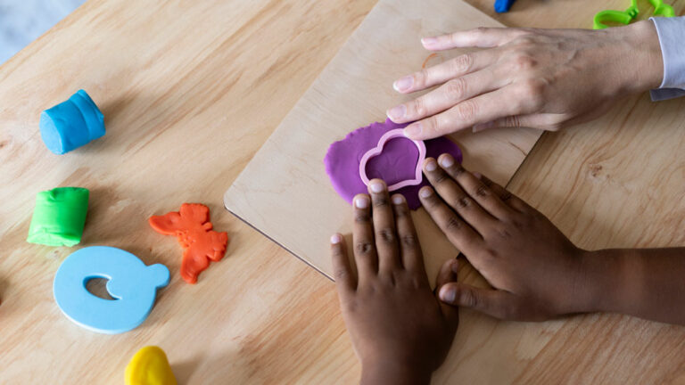 Child care teacher and student cutting shapes out of play-doh
